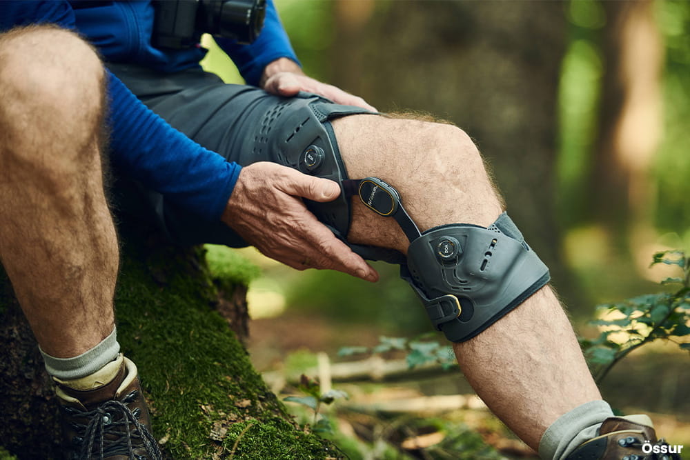 Ein Mann sitzt im Wald und legt seine Hände um eine Beinorthese