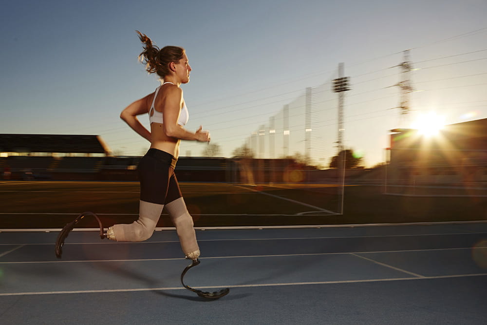 A female athlete with 2 sports prostheses runs on the running track at sunset.