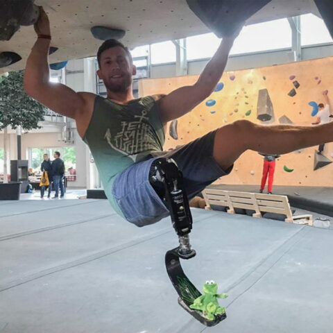 Junger Mann mit Oberschenkelprothese hängt an einer Boulderwand und klettert.