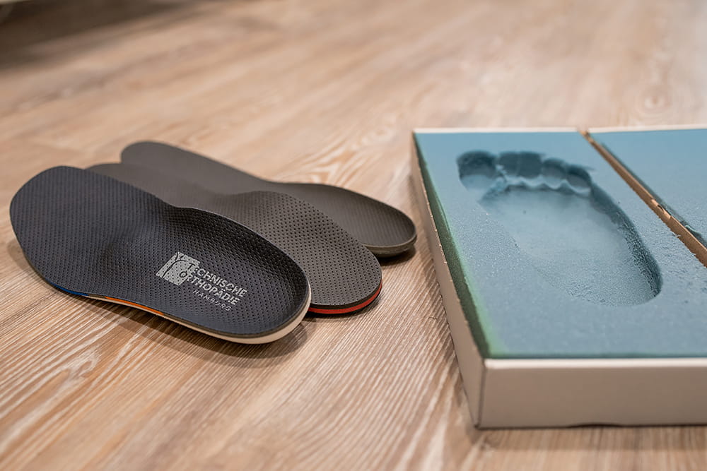 Ein Fußabdruckschaum liegt auf dem Boden mit einem frischen abdruck und daneben liegen 3 Schuheinlagen.