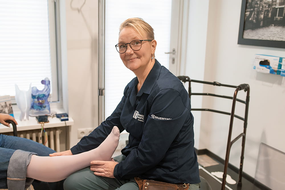 Eine Mitarbeiterin des Sanitätshauses hilft gerade einer Kundin und schaut dabei in die Kamera.