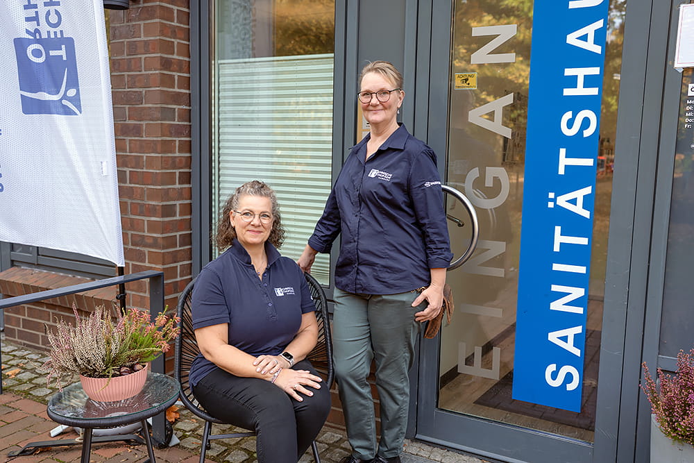 Zwei Mitarbeiter der TOH stehen und sitzen entspannt vor dem Laden des Orthopädiehauses.