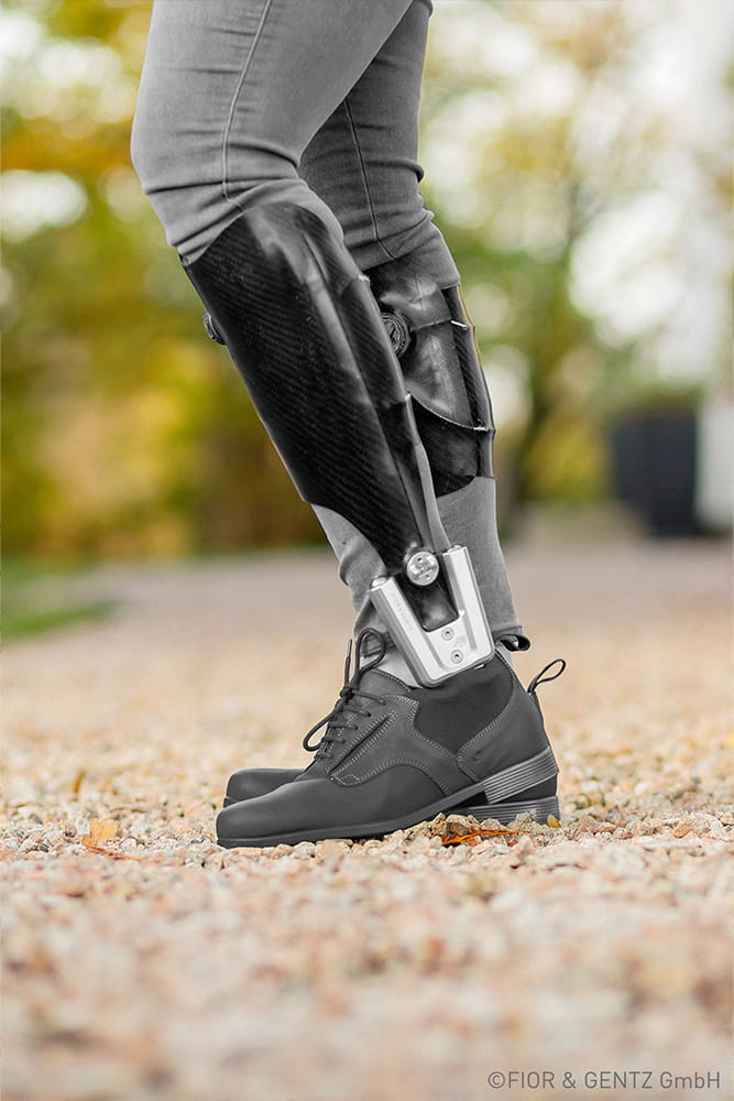 Ein Mann trägt eine schwarze Beinorthese über seiner Hose und dazu stylische dunkle Orthesenschuhe.
