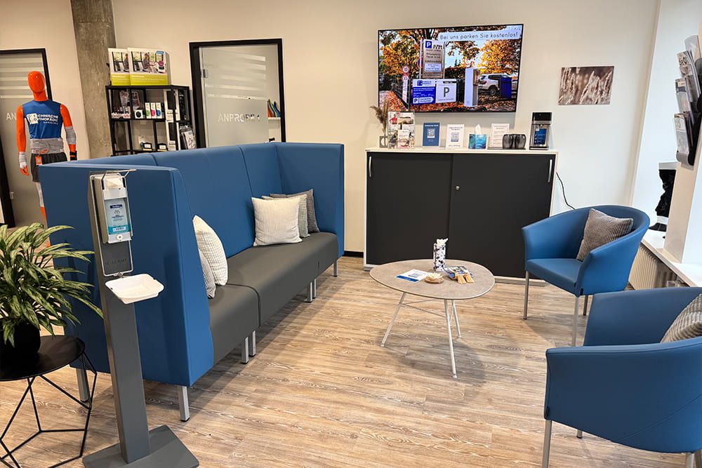 Wartebereich des Sanitätshauses der Technischen Orthopädie Hamburg mit blauen Postermöbeln, einem kleinen Tisch und einem Info-TV.